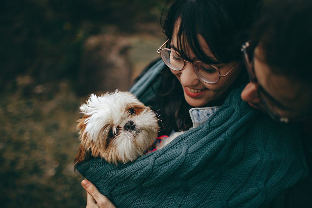 A woman lovingly cuddles her Shih Tzu puppy, wrapped in a warm blanket outdoors in a dog-friendly park